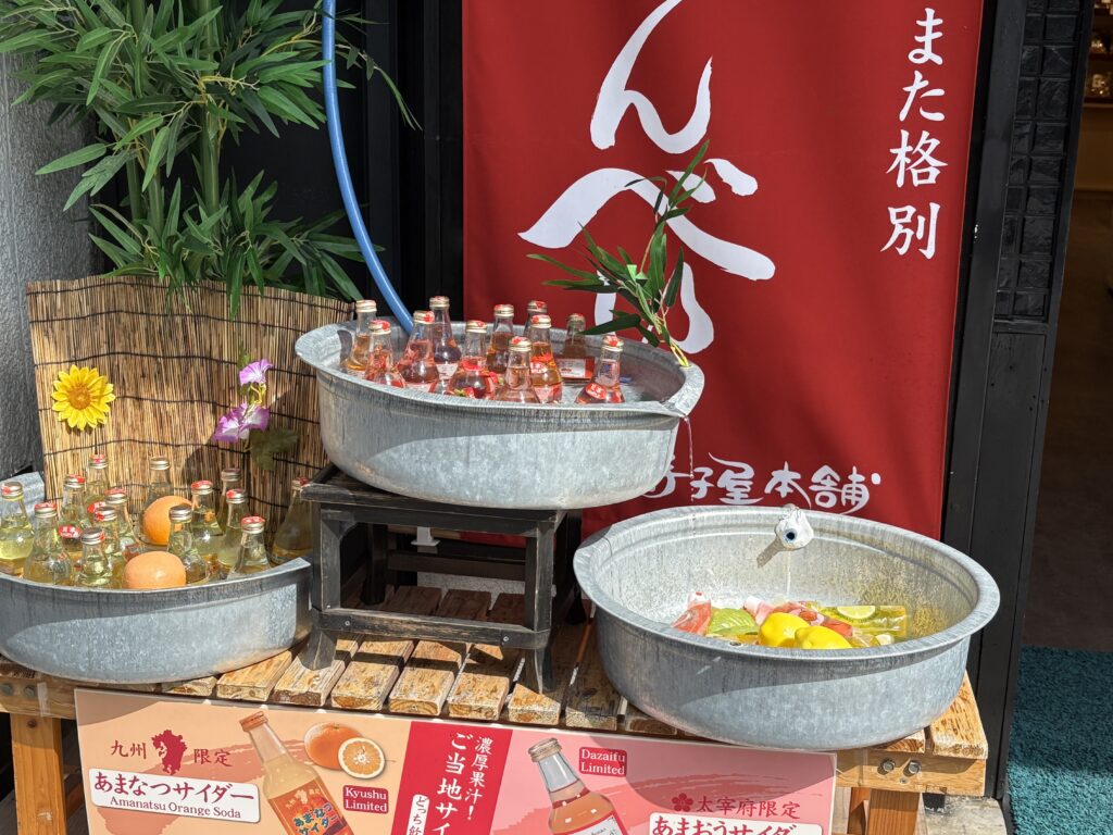 太宰府参道に並ぶあまなつサイダーやあまおうサイダーなど、色とりどりの瓶が桶に冷やされている様子。