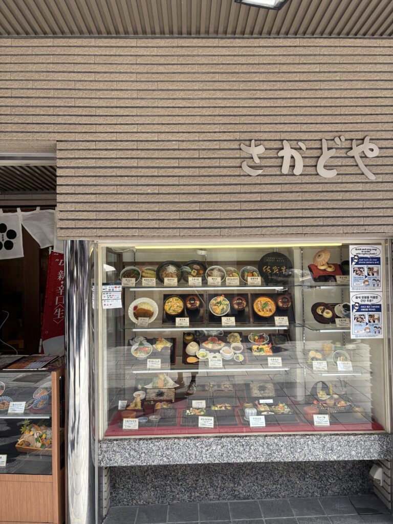 太宰府参道沿いの食事処『さかどや』の外観。ショーウィンドウにはうどんや定食の食品サンプルが並び、観光客に人気