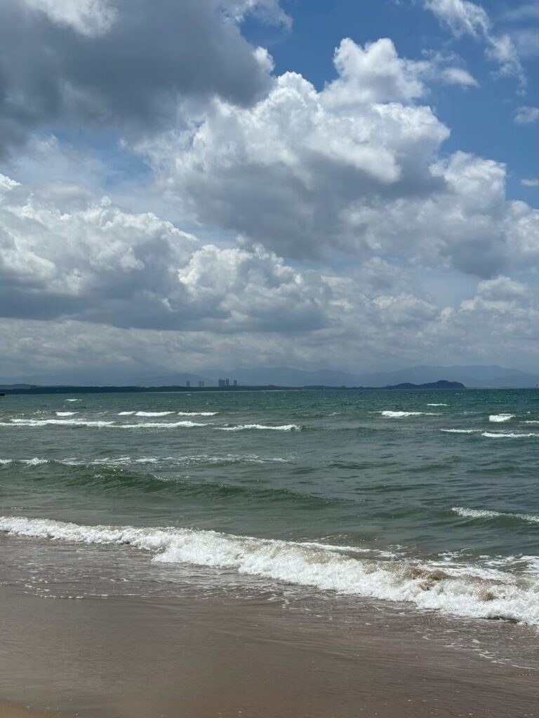 雲の合間から光が差す福間海岸。穏やかな波と風が心地よい午後の海。